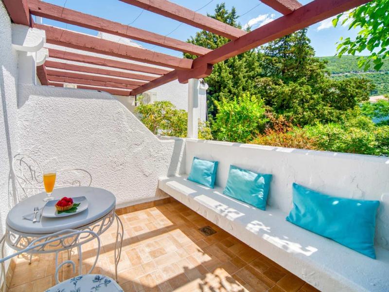 Acogedora terraza con cojines azules, mesa redonda y zumo de naranja fresco en jardín soleado del hotel.
