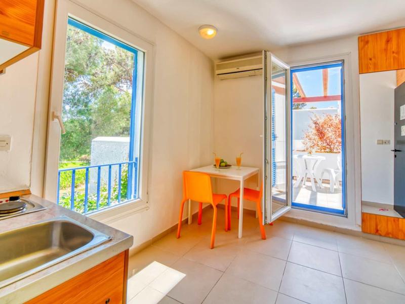 Área de cocina y comedor luminosa con ventana, puerta al balcón y mobiliario sencillo.