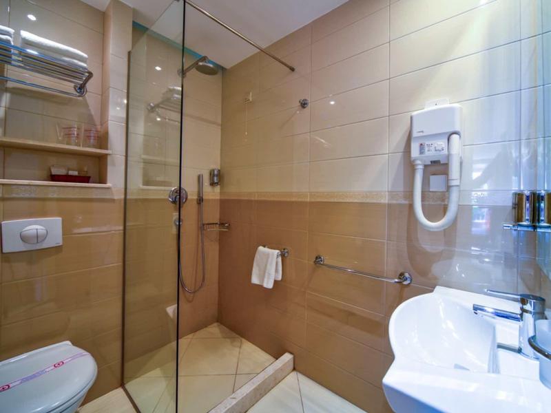 Baño luminoso con ducha de vidrio, lavabo, inodoro y secador de pelo en la pared.