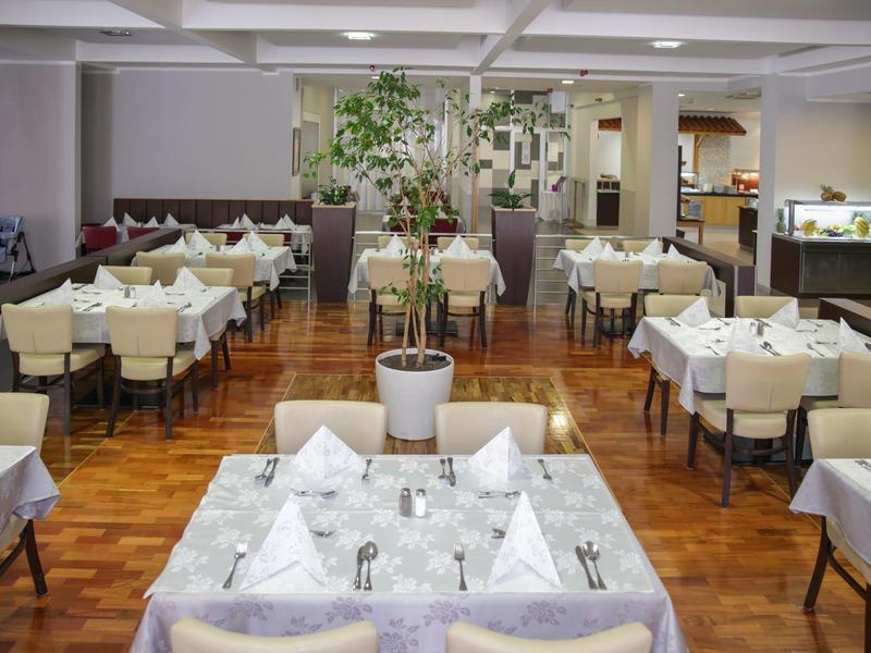 Ristorante luminoso con tovaglie bianche, sedie e una grande pianta in vaso al centro.