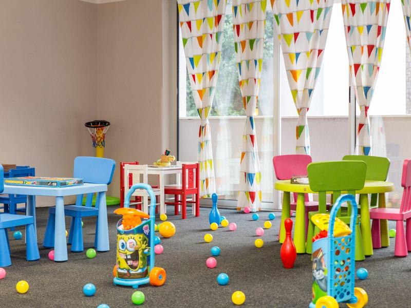 Sala giochi colorata per bambini con piccoli tavoli, sedie e palline di plastica sparse.