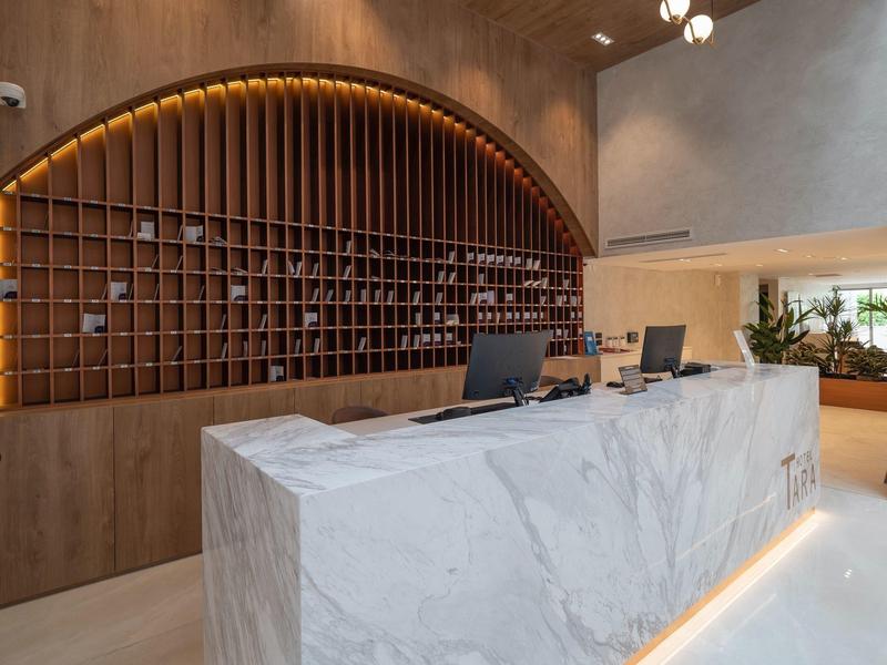 Reception moderna di hotel con bancone in marmo e portachiavi in legno a parete.