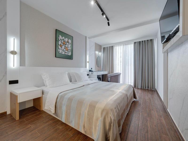 Camera d'hotel moderna con letto grande, scrivania e TV a muro.