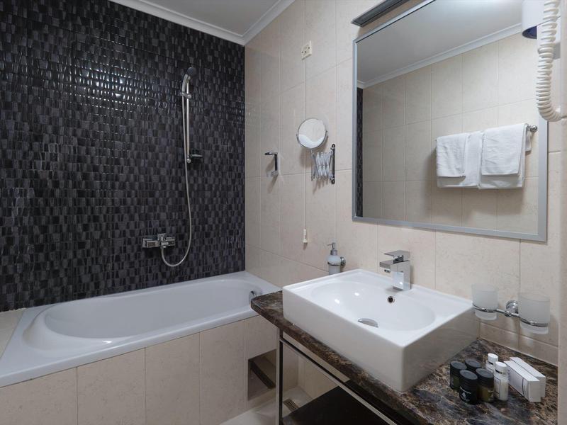 Bagno moderno con vasca da bagno, parete d'accento scura e grande specchio sopra il lavabo bianco.