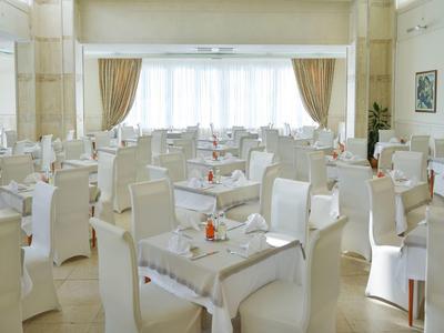 Helles Restaurant mit weißen Stühlen, Tischen, großen Fenstern und hellen Vorhängen.