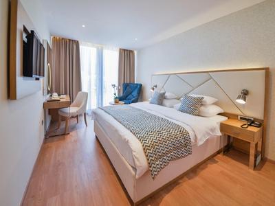 Modernes Hotelzimmer mit Doppelbett, Holzfußboden, TV, Schreibtisch und gemütlichem Sessel.