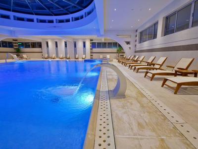 Innenpool mit blauer Beleuchtung und Liegestühlen in modernem Hotel.