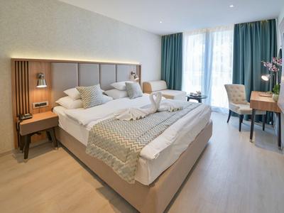 Modernes Hotelzimmer mit einem Doppelbett, Schreibtisch, Stuhl und großen Fenstern mit Vorhängen.