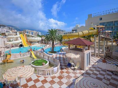 Bunter Wasserpark mit Rutschen, Pool und Palmen vor einem Hotelgebäude bei sonnigem Himmel.