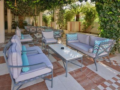 Gemütliche Terrasse mit grauer Sitzgarnitur, blauen Kissen und grünen Pflanzen im Hintergrund.