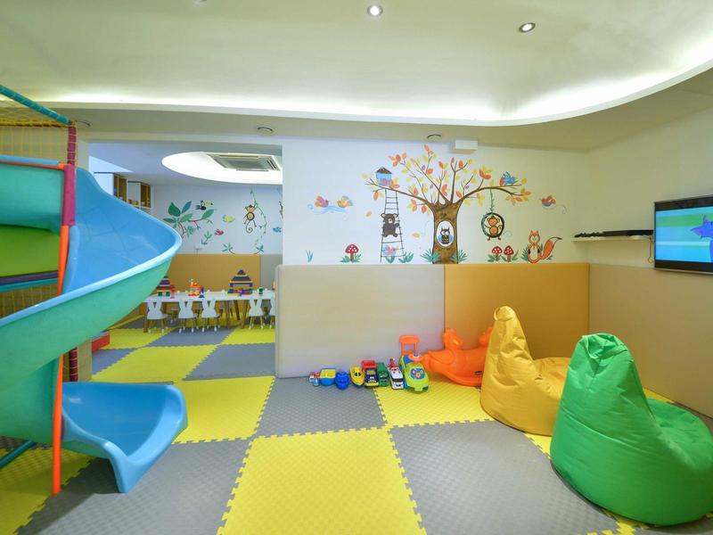 Kinderspielzimmer mit bunter Rutsche, weichen Sitzsäcken und gepolstertem Boden in Gelb, Grau und Grün.