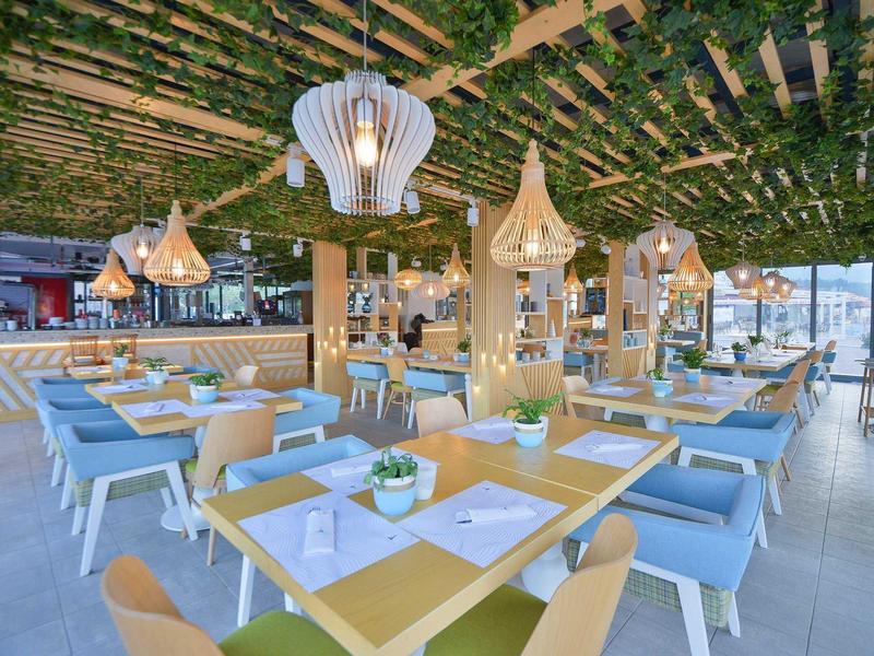 Moderner Außenbereich eines Restaurants mit hölzernen Tischen, blauen Stühlen und dekorativen Lampen.