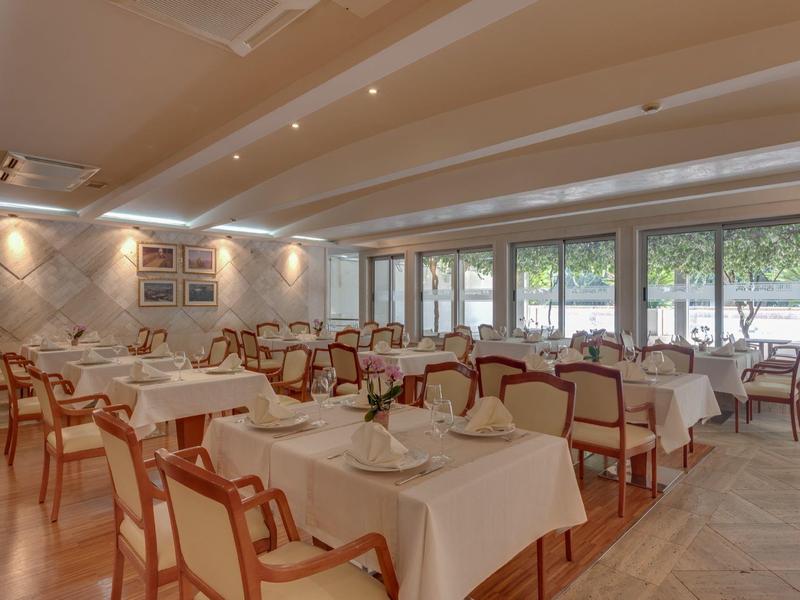 Helles Restaurant mit weißen Tischdecken, Holzstühlen und großen Fenstern mit Blick ins Grüne.