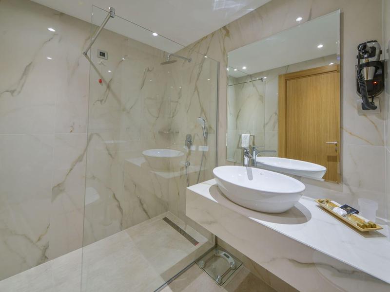 Moderne Badezimmerecke mit Glasdusche, rundem Waschbecken und großem Spiegel, helle Marmoroptik.