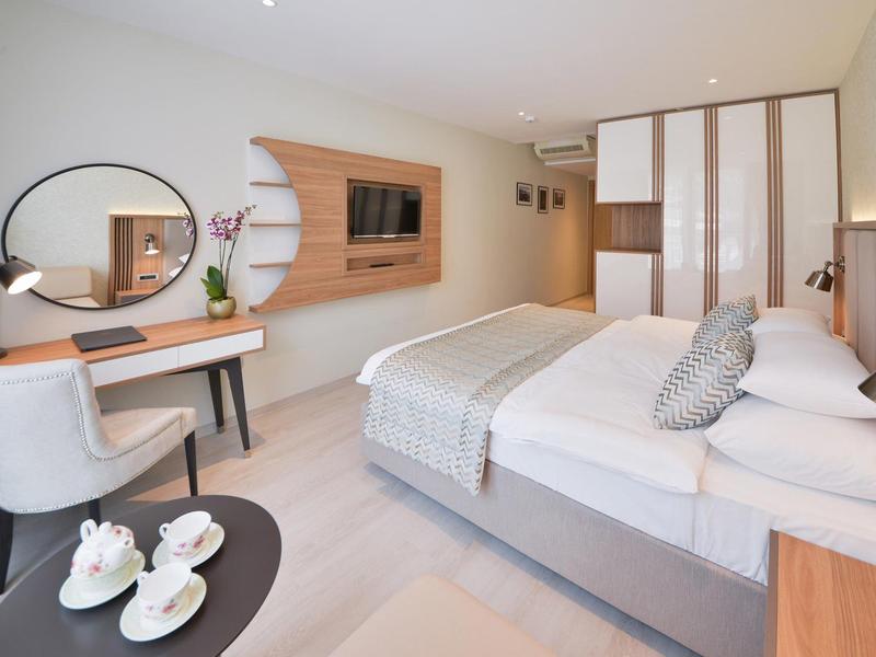 Modernes Schlafzimmer mit großem Bett, Holzschrank, runder Spiegel und elegantem Schminktisch.