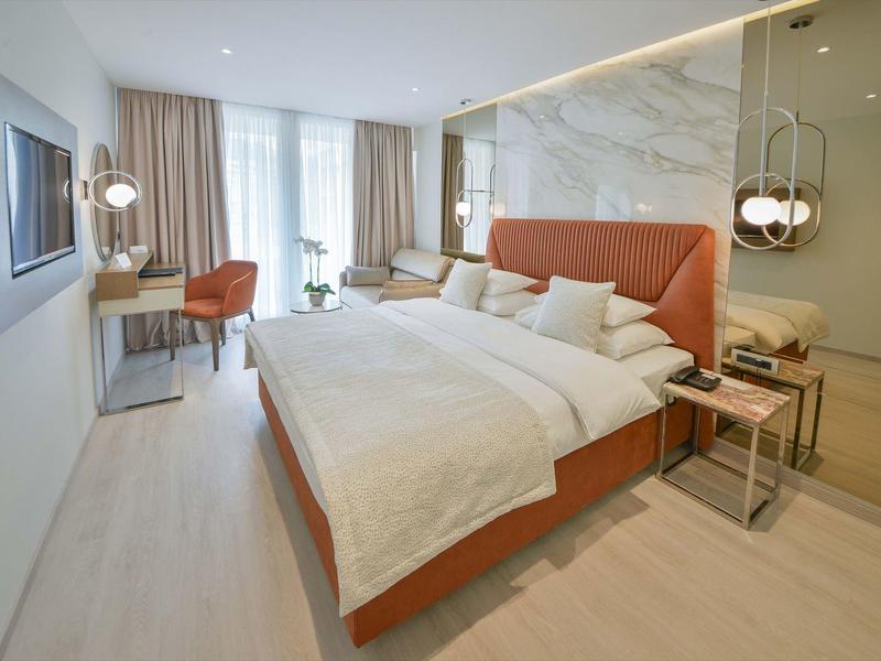 Modernes Hotelzimmer mit großem Bett, Schreibtisch, Sesseln und hellen Vorhängen.