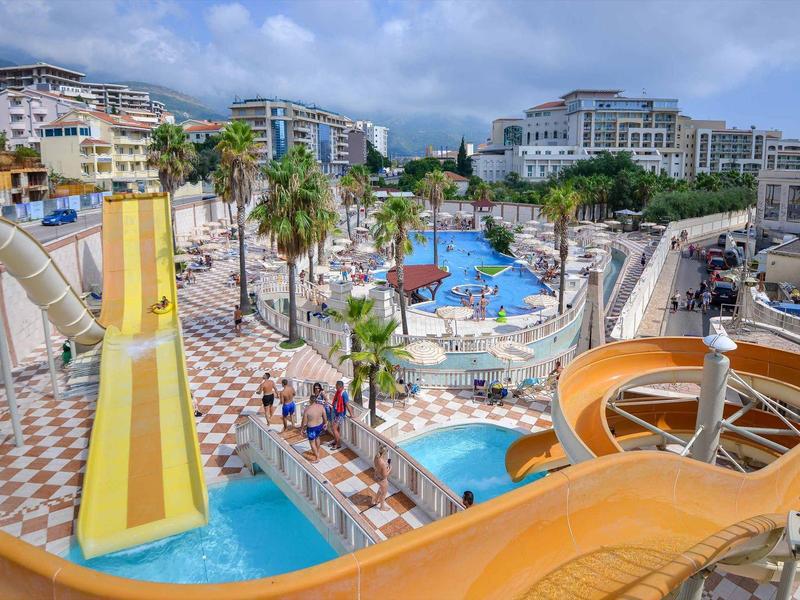 Wasserpark mit Rutschen, Pools, Palmen und umliegenden mehrstöckigen Gebäuden bei klarem Himmel.