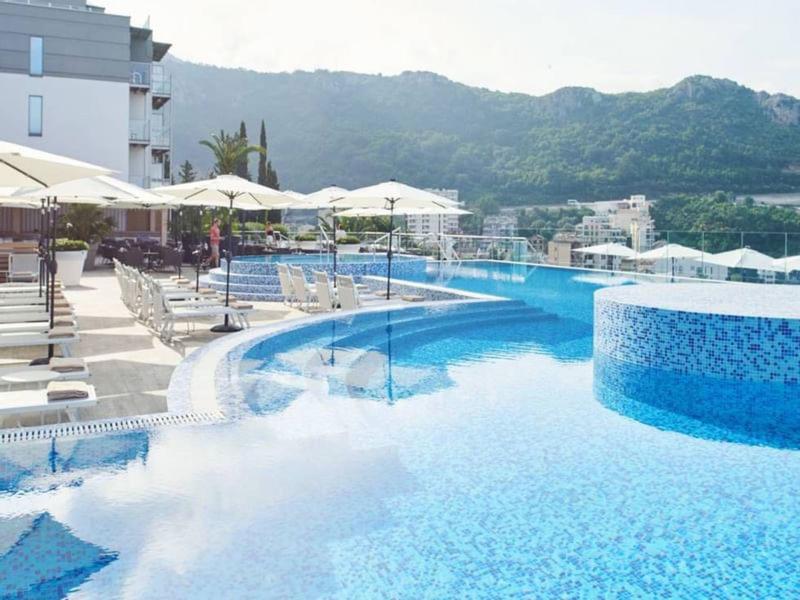 Großer Außenpool mit Terrassen, Sonnenschirmen und Bergblick bei klarem Himmel.
