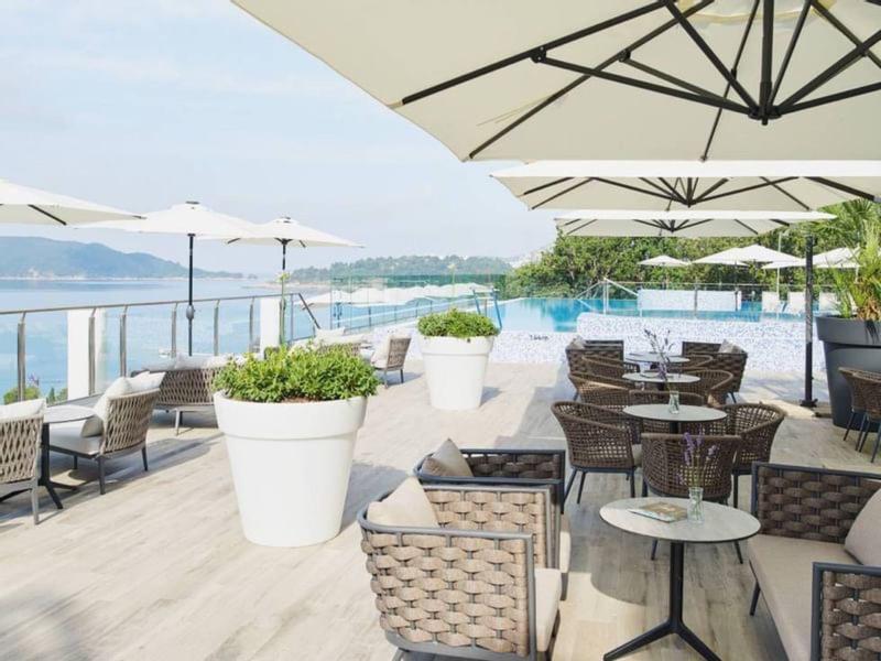 Terrassenbereich mit Tischen, Stühlen, weißen Sonnenschirmen und großer Pflanzendeko am Wasser.