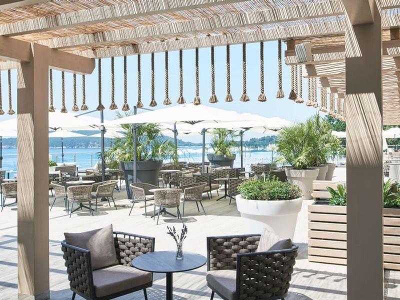 Terrasse mit Holzdach, modernen Sesseln, Tischen und Blick auf Wasser und Berge im Hintergrund.