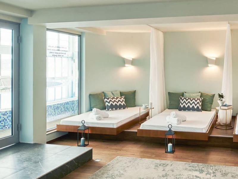 Helles Zimmer mit zwei niedrigen Betten, großen Fenstern und modernem Wandlicht.