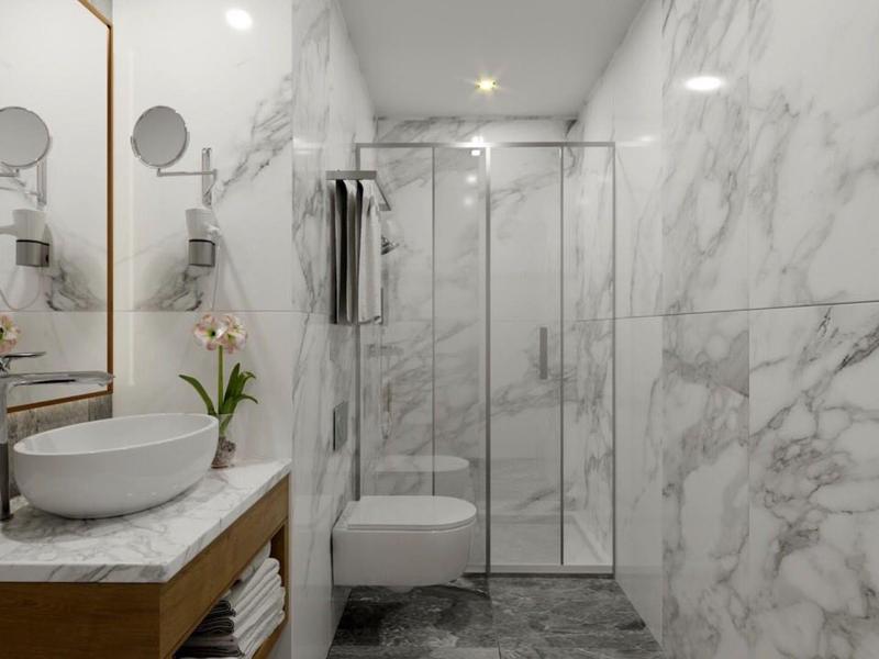 Moderní koupelna s mramorovými dlaždicemi, skleněným sprchovým koutem a umyvadlem s velkým zrcadlem.