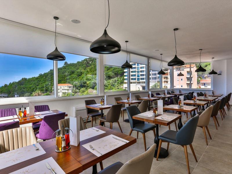 Světá jídelna s moderním nábytkem a velkými okny s výhledem na zelené kopce.