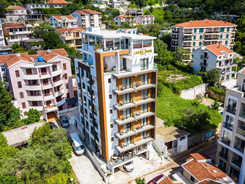 Vícepodlažní hotelová budova s balkony v zelené, kopcovité oblasti.