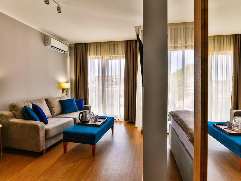 Moderně zařízený hotelový pokoj s pohovkou, stolem a velkými okny s závěsy.