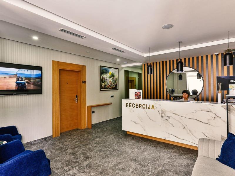 Moderní recepce s mramorovou přepážkou, židlemi a kulatým zrcadlem na zdi.