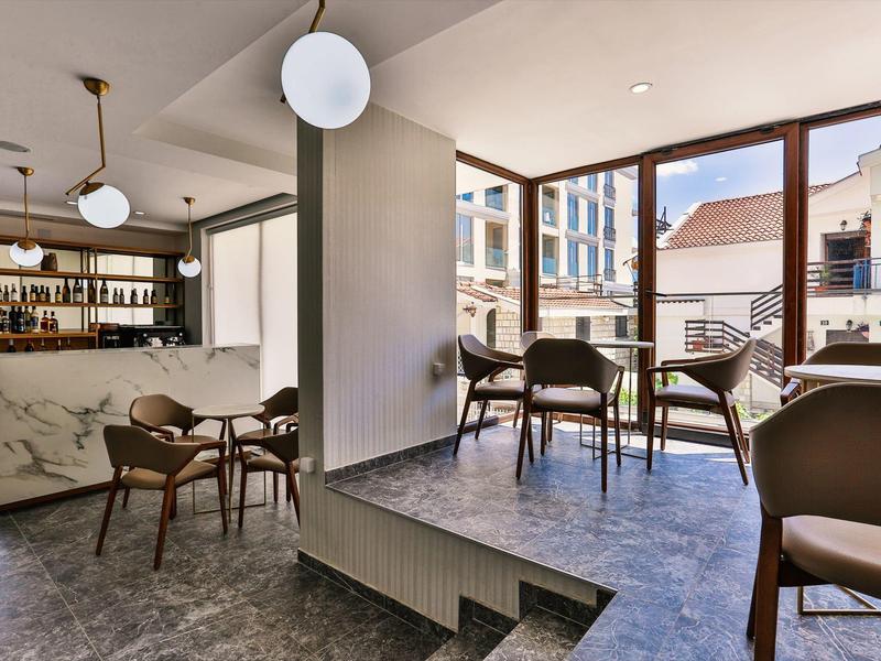 Moderní hotelový bar s posezením u velkých oken s výhledem na město.