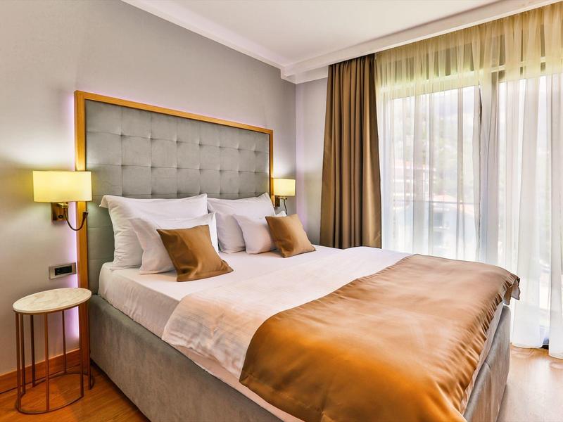 Pohodlný hotelový pokoj s velkou postelí, béžovými a hnědými akcenty a okny od podlahy ke stropu