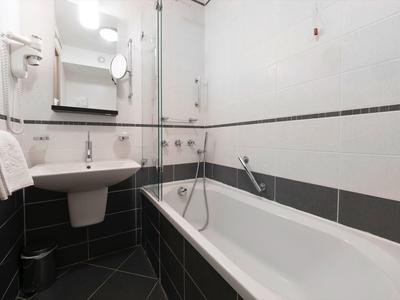 Baño moderno con bañera, lavabo, espejo y toallero en tonos grises.