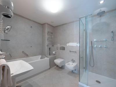 Baño moderno con ducha, bañera, lavabo y sanitario en tonos claros.