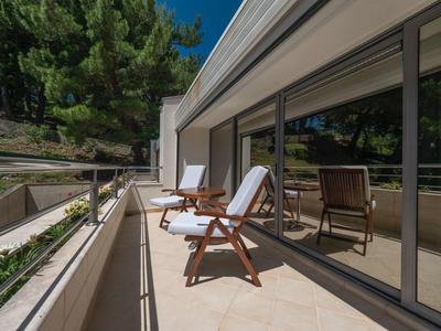 Balcón con muebles de madera y ventanas de vidrio liso en una habitación de hotel con vista a árboles.