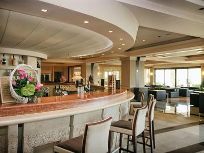 Bar elegante en hotel con mostrador de madera, arreglo floral y asientos altos en espacio luminoso.