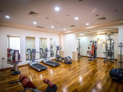 Ein gut beleuchteter Fitnessraum mit Laufbändern, Hanteln und Kraftgeräten auf Holzfußboden.