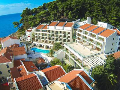 Complejo hotelero en la costa con varios edificios, piscina y vista al mar bajo cielo azul.