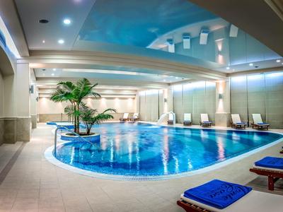 Piscina interior con iluminación suave, plantas y tumbonas en un entorno de hotel relajante.