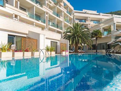 Moderner Hotelpool mit umgebenden Balkonen und Palmen unter klarem blauem Himmel.