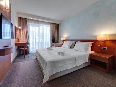 Habitación de hotel con cama doble, escritorio, lámpara y balcón con cortinas claras.