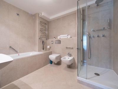 Baño moderno con bañera, ducha, inodoro y bidé en tonos neutros.