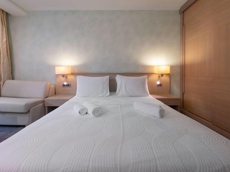 Habitación de hotel acogedora con cama grande, ropa de cama blanca y sofá junto a la ventana.