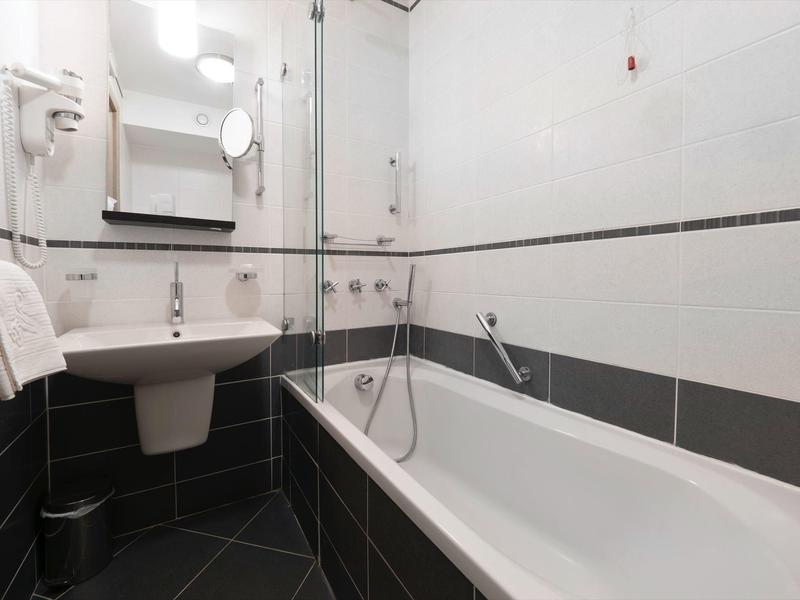 Baño moderno con bañera, lavabo, espejo y toallero en tonos grises.