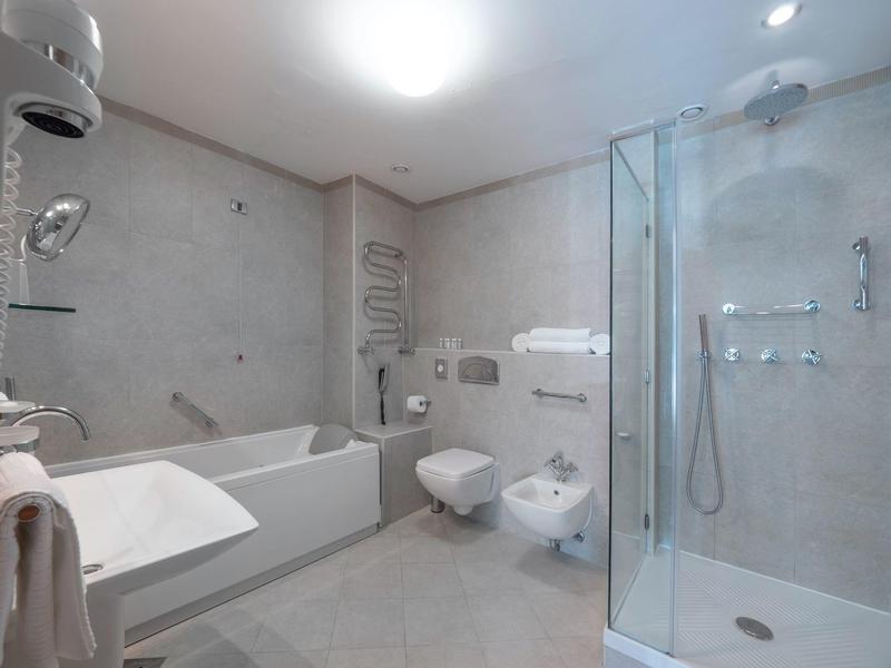 Baño moderno con ducha, bañera, lavabo y sanitario en tonos claros.