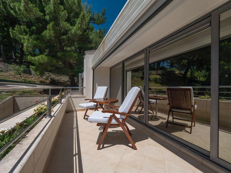 Balcón con muebles de madera y ventanas de vidrio liso en una habitación de hotel con vista a árboles.