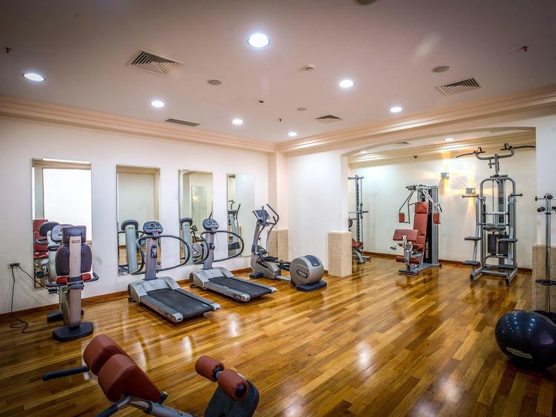 Gimnasio luminoso con suelo de madera, cintas de correr y varias máquinas de fuerza.