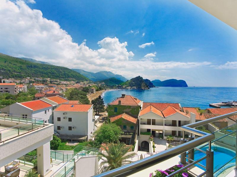 Vista desde el balcón de un pueblo costero con techos rojos y mar azul bajo cielo soleado.