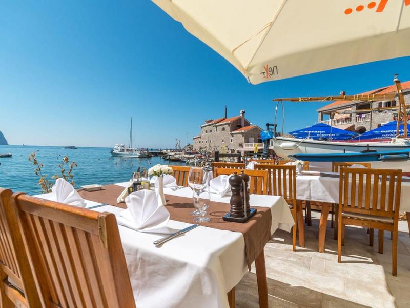 Terraza de restaurante con mesas de madera y vista al puerto bajo un cielo soleado.