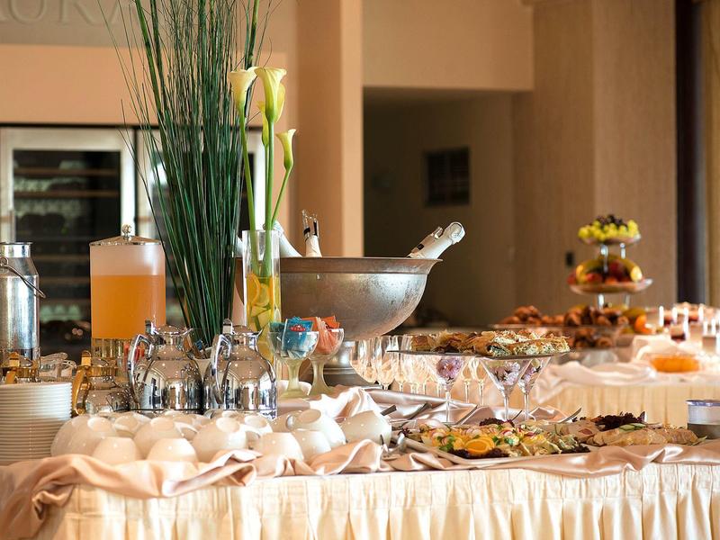 Una mesa de desayuno preparada con bebidas, vasos y diferentes alimentos en un hotel.